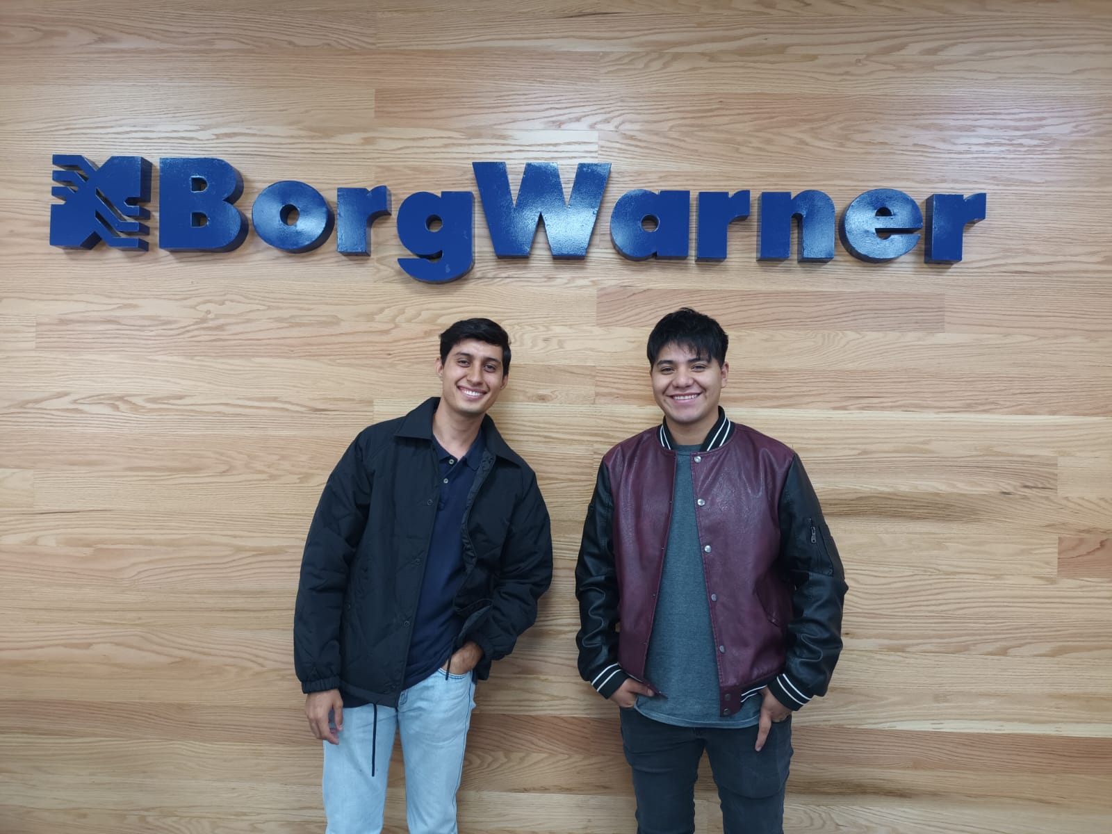 two young men standing under a BorgWarner logo