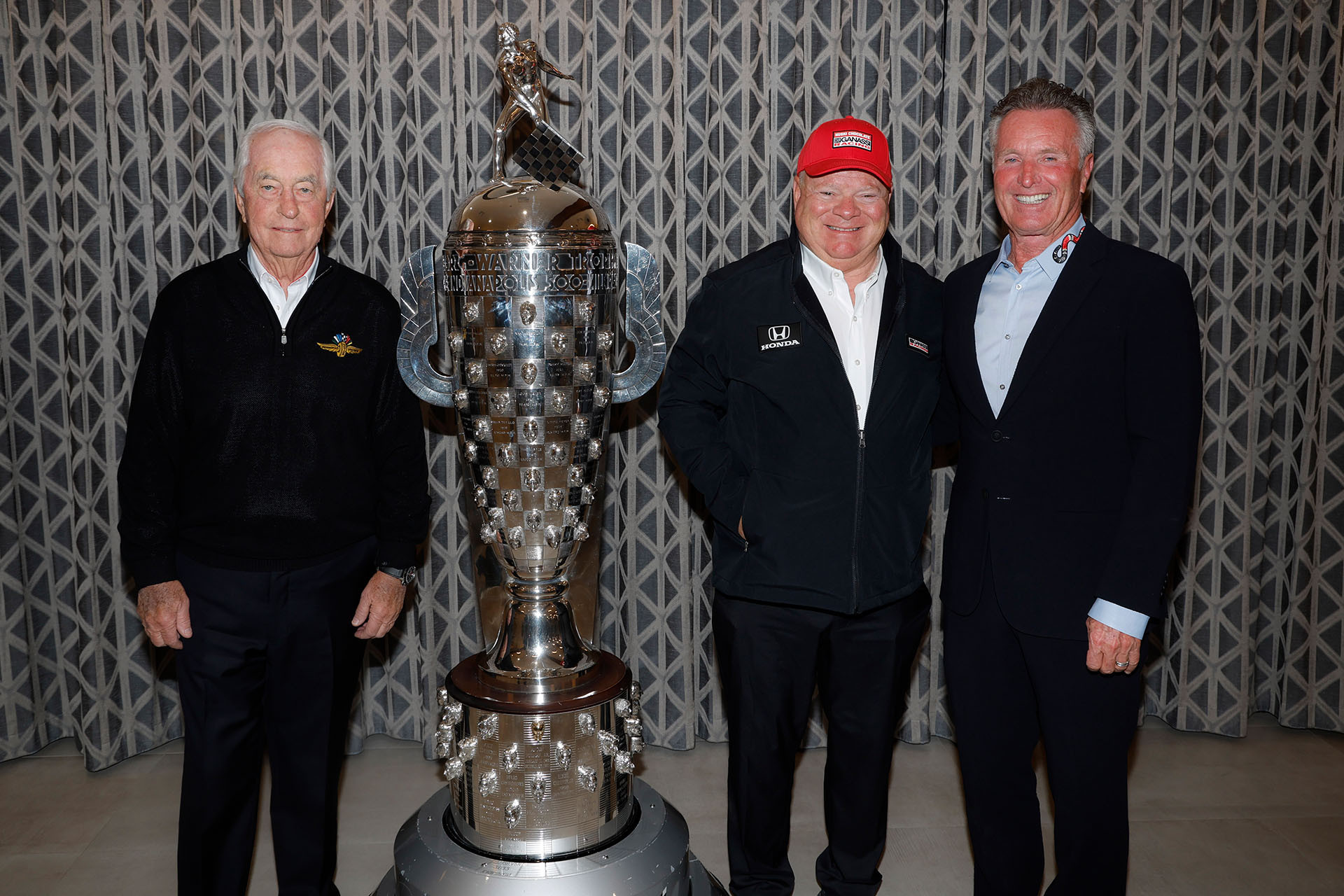 Three people stand in line next to large silver trophy while smiling