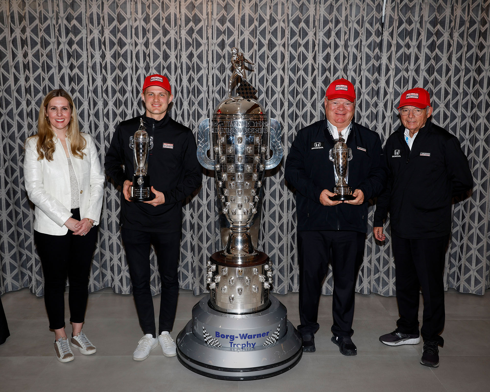 Four people stand in line next to large silver trophy while smiling