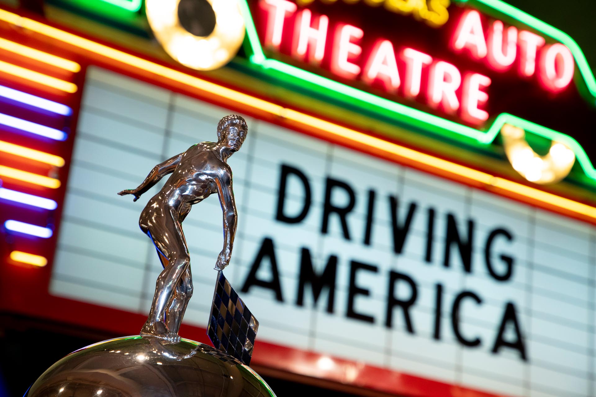 Metal man on large silver trophy in front of marquee sign
