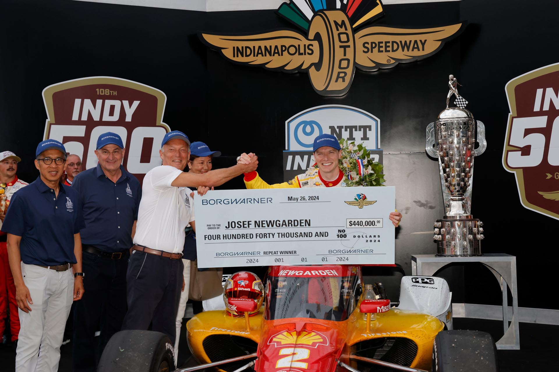 A group of men proudly holding a large check celebrating their Indy 500 race achievement.