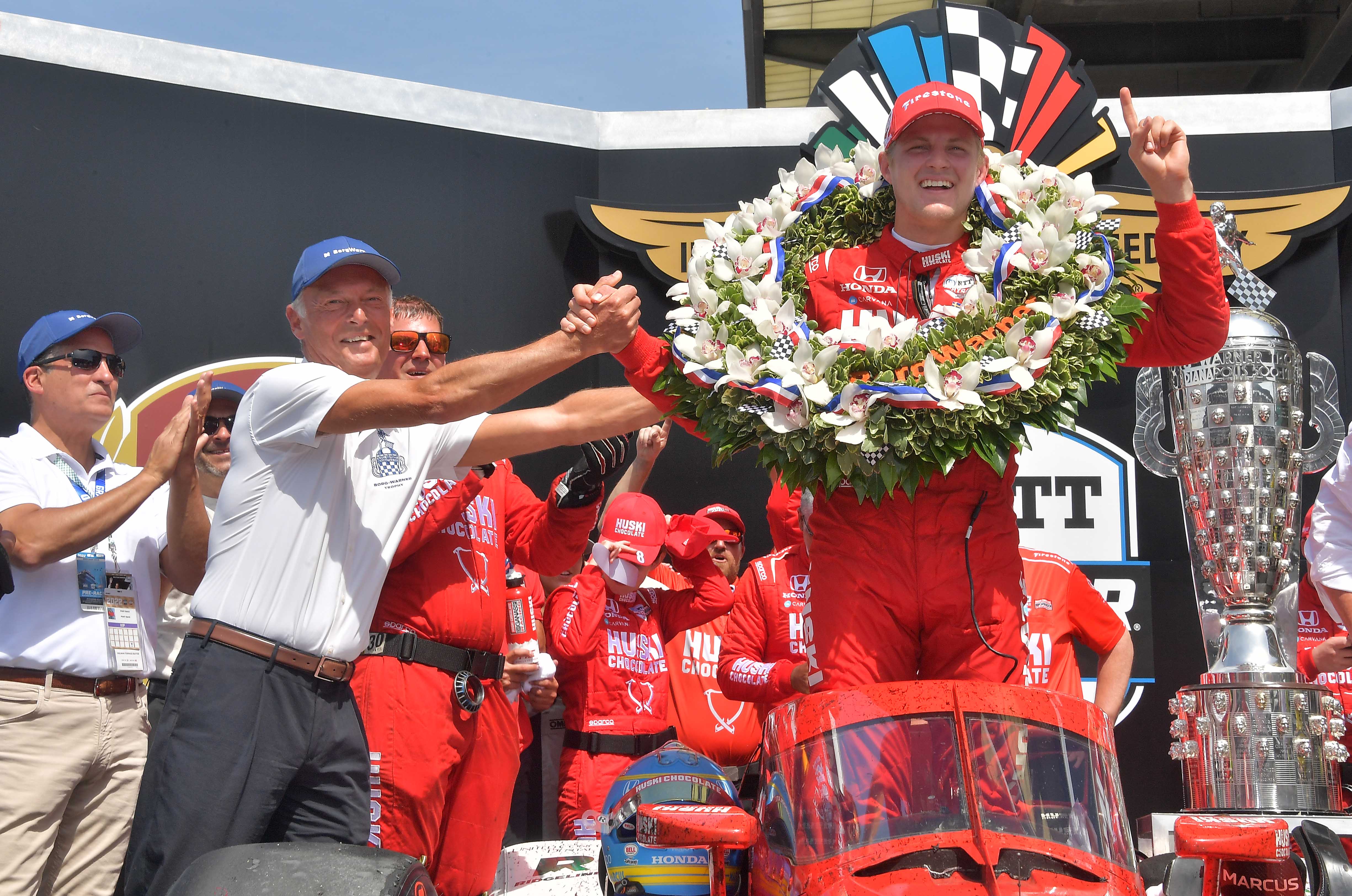 Man awards driver in red track suit with wreath and trophy