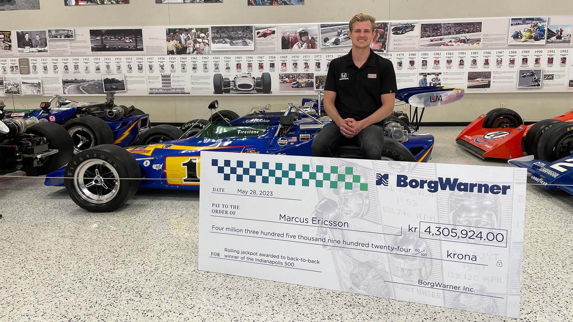 Man sits with giant check in racing history museum