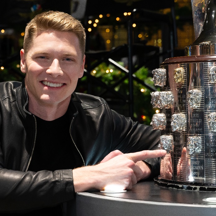 Man smiles and points at art deco silver trophy