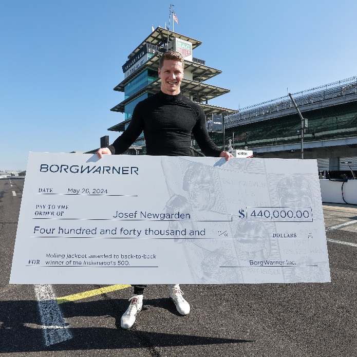 Man in black shirt on speedway track holds large check for $440,000