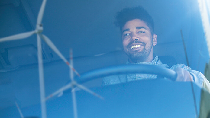 Man driving a commercial vehicle, wind energy turbines reflecting in the windshield